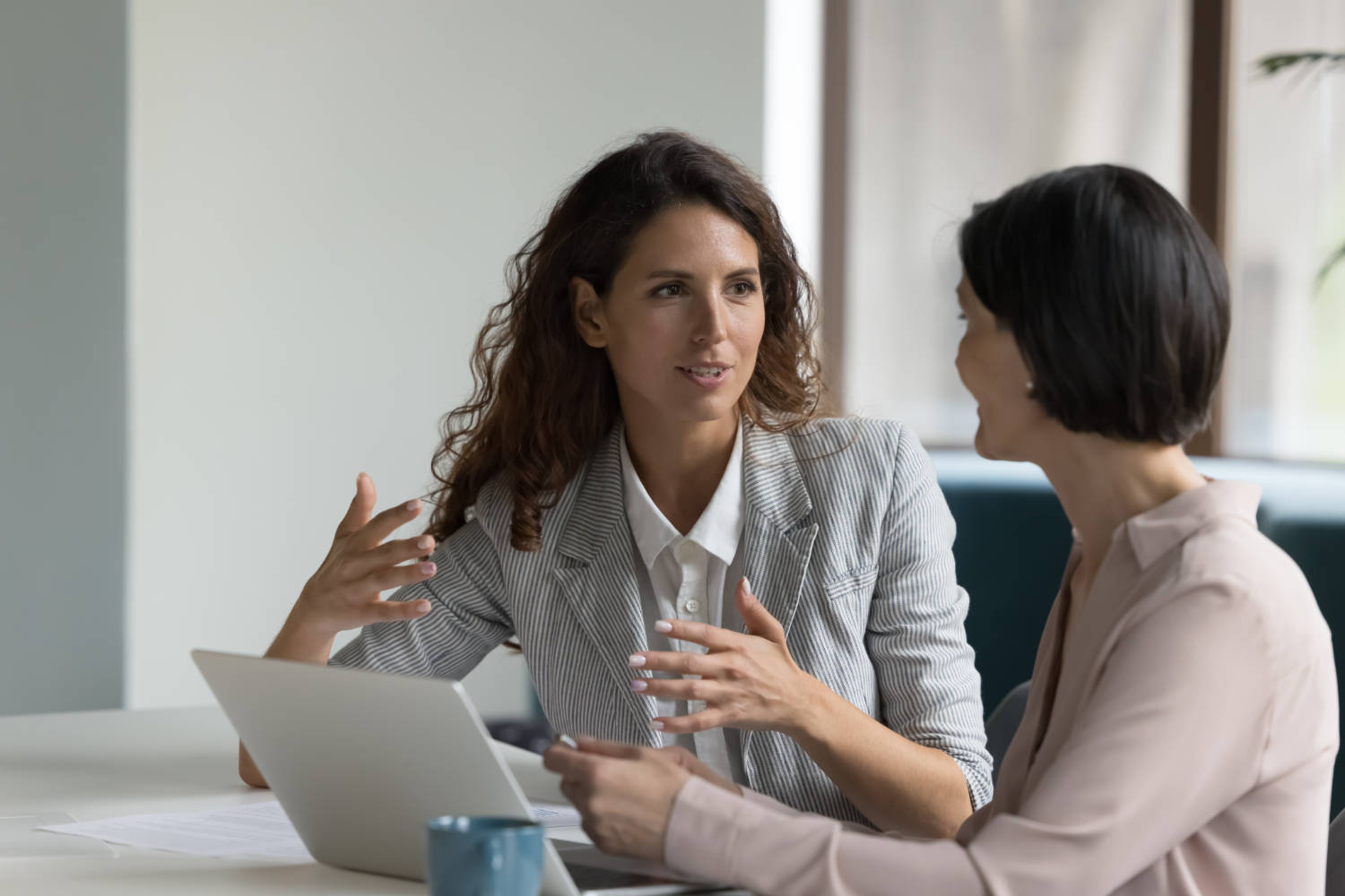 Two,Business,Women,Sit,At,Desk,Discuss,Project,Details,,Diverse